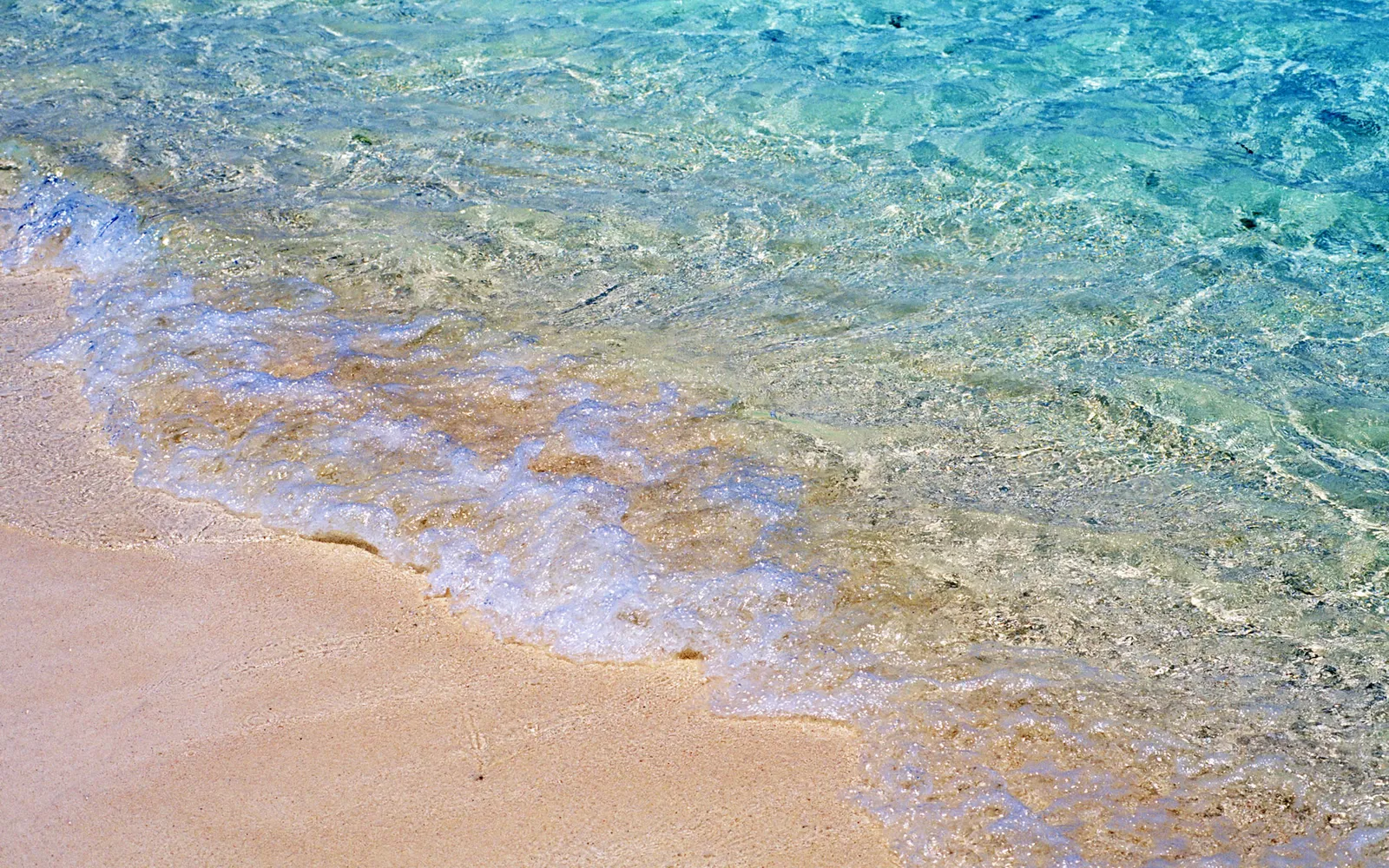A gentle wave laps onto a sandy beach with clear turquoise water.