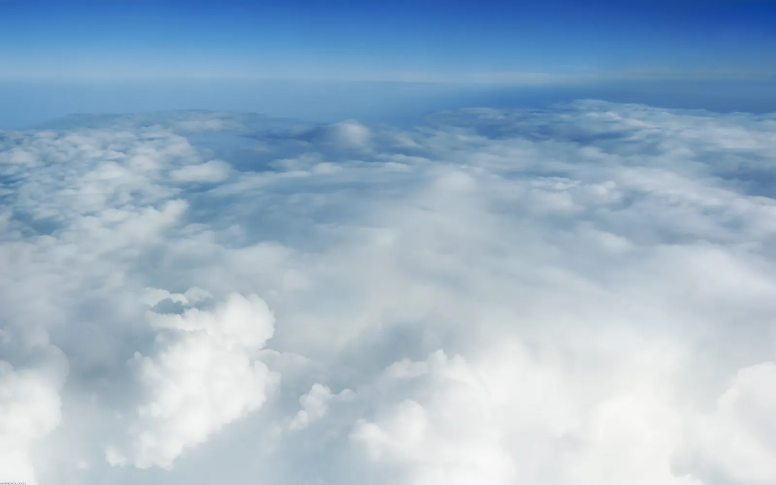 View from above the clouds, showing a vast expanse of white and grey clouds under a clear blue sky.