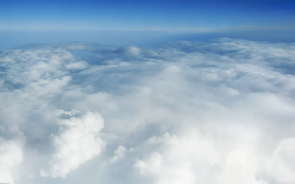 View from above the clouds, showing a vast expanse of white and grey clouds under a clear blue sky.