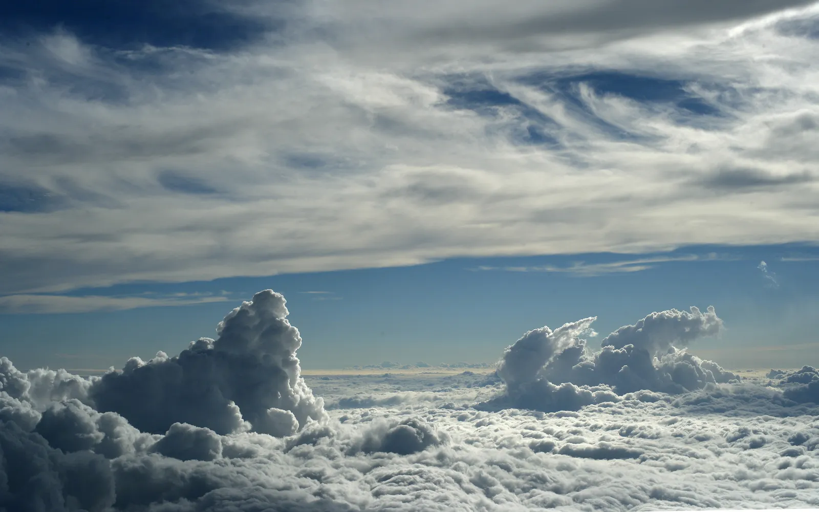 A vast expanse of white clouds stretches to the horizon, with dramatic cumulus clouds in the foreground and wispy cirrus clouds in the blue sky above.