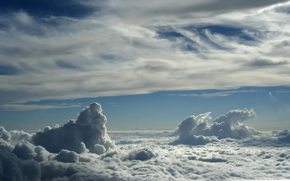 A vast expanse of white clouds stretches to the horizon, with dramatic cumulus clouds in the foreground and wispy cirrus clouds in the blue sky above.