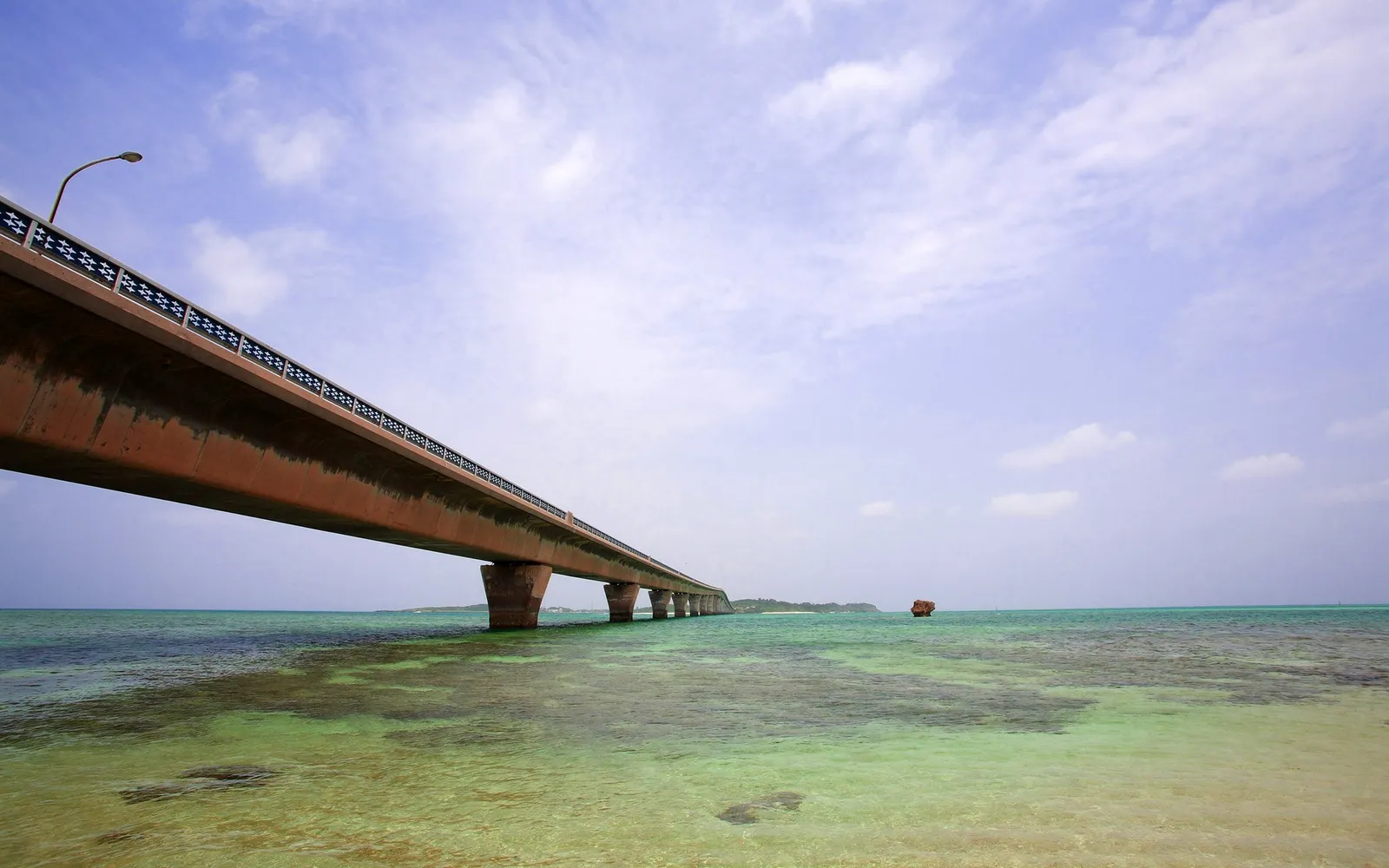 A long concrete bridge extends over clear turquoise water with a small island in the distance.