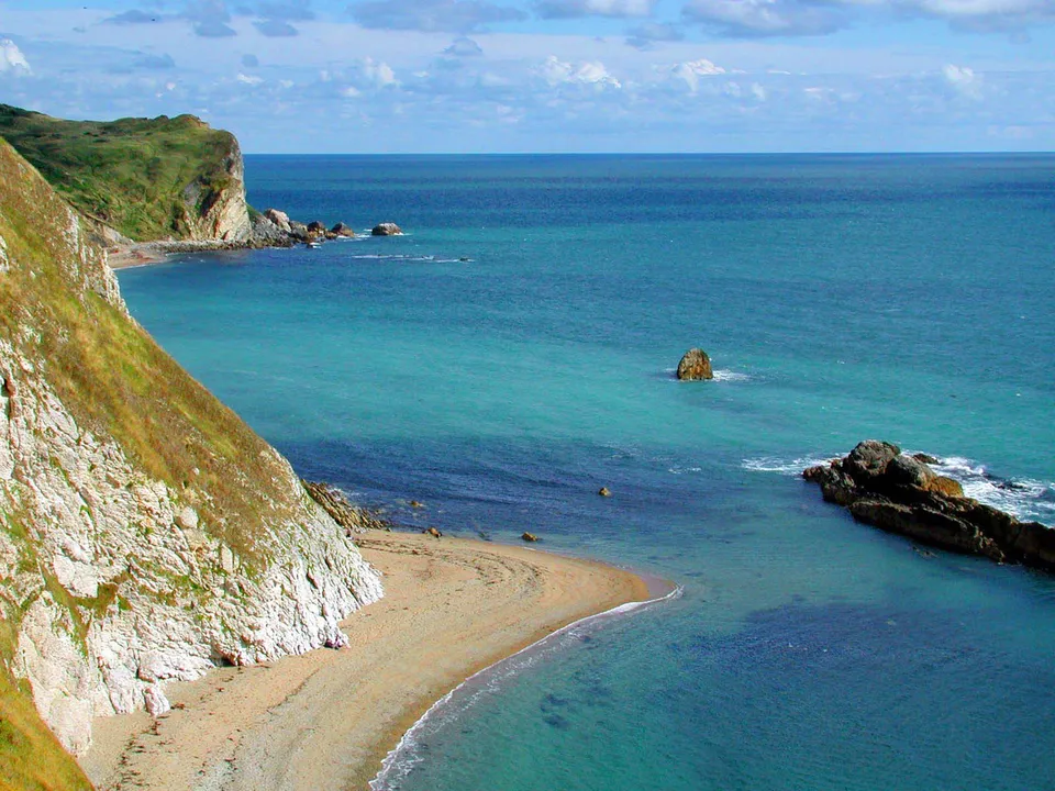 A view of rugged green and white cliffs meeting the clear turquoise sea with a small sandy beach.