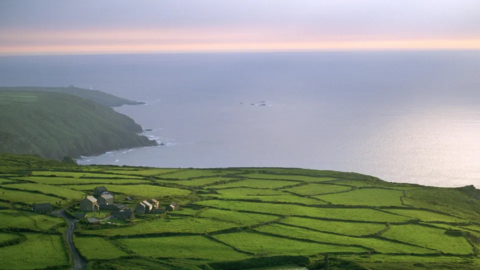 A view of green patchwork fields leading to a rugged coastline and the ocean at dusk.