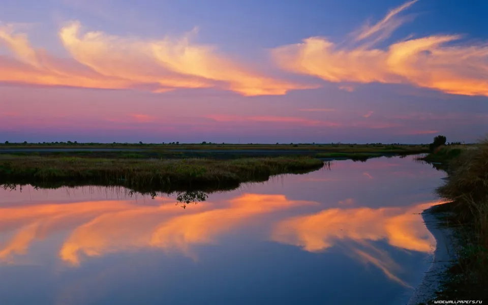A tranquil coastal marsh reflects the blue and orange hues of a sunset sky.
