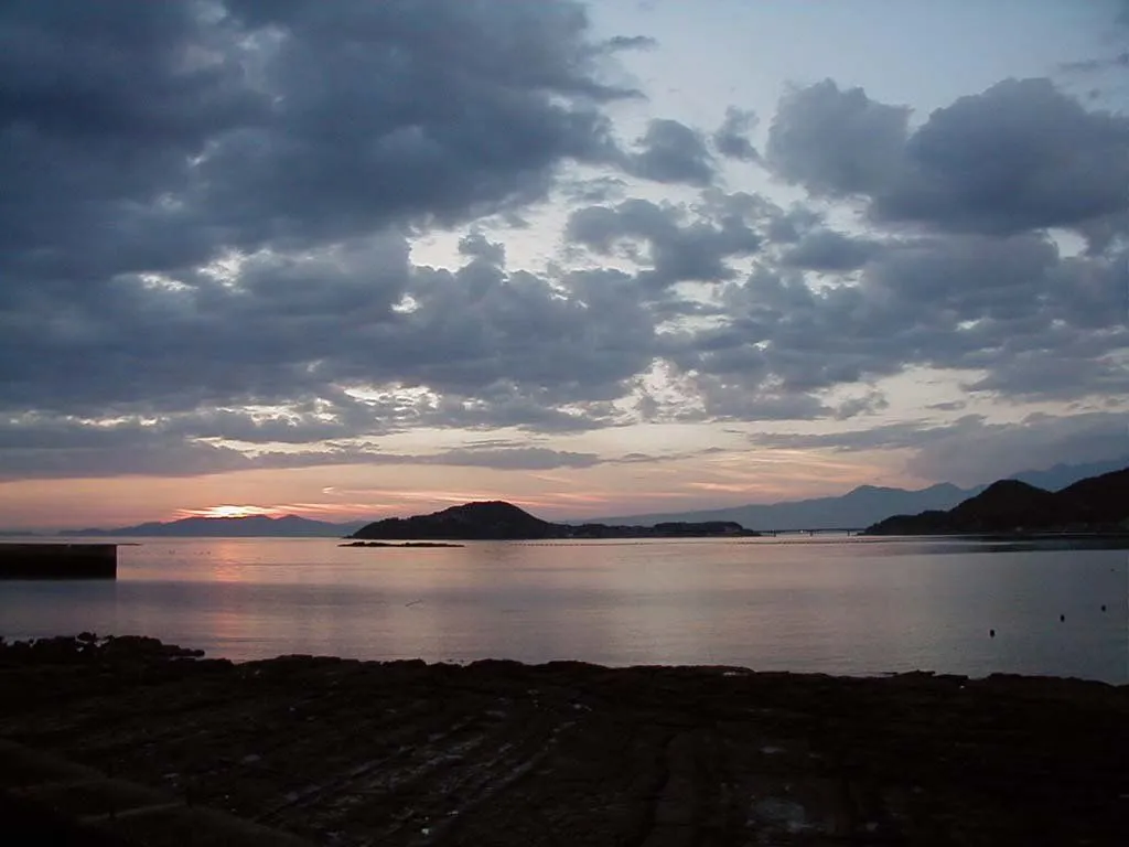 A dramatic sunset with colorful clouds over a calm ocean and distant mountains.