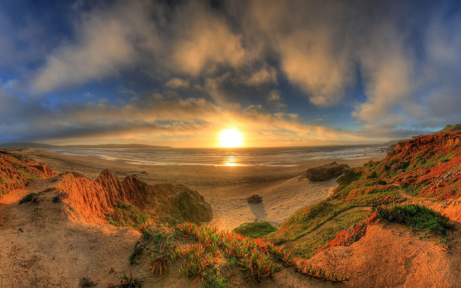 A vibrant sunset over the ocean, with colorful clouds and a sandy beach in the foreground.