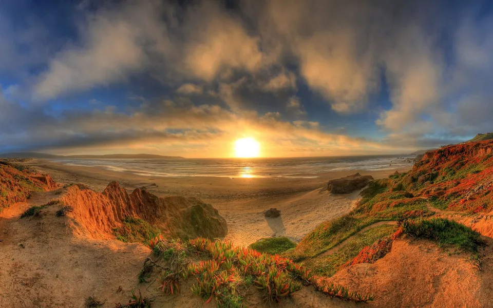 A vibrant sunset over the ocean, with colorful clouds and a sandy beach in the foreground.