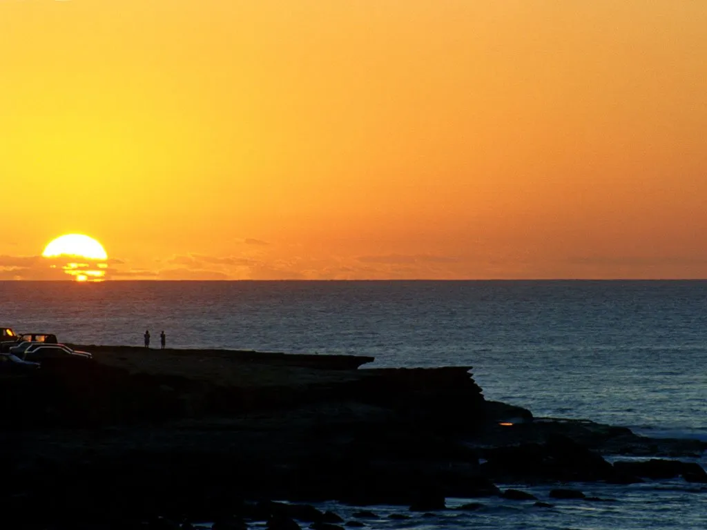 The sun is setting over the ocean, casting a warm golden glow across the sky and water.