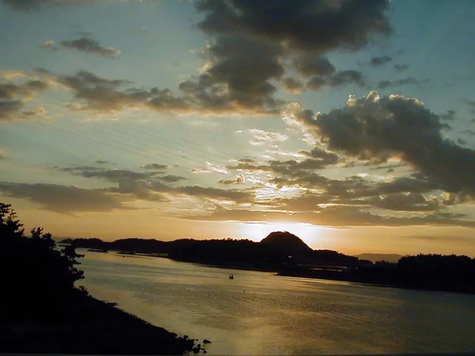 A wide body of water reflects the golden light of a sunset behind a silhouetted hill.