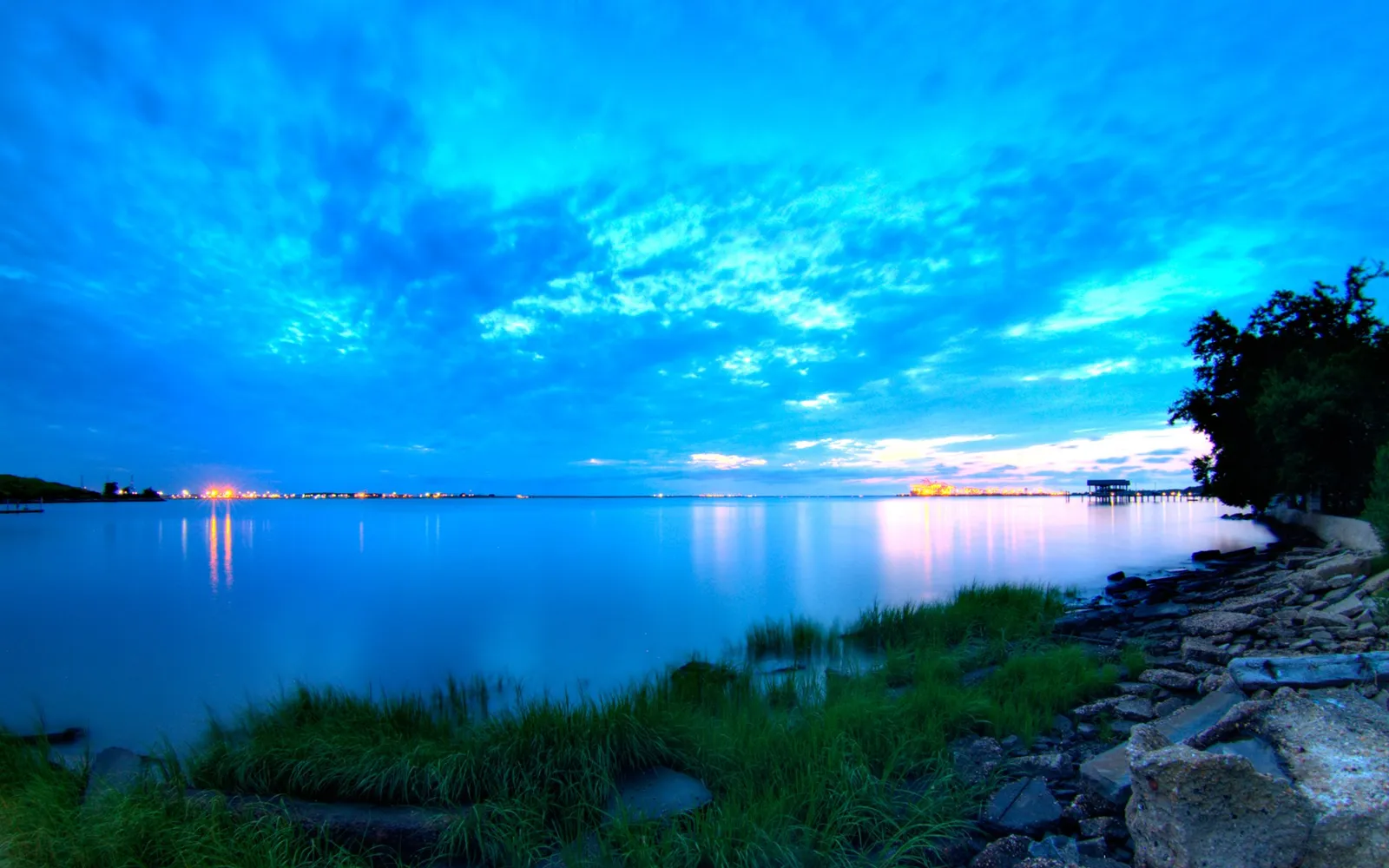 A wide expanse of calm water reflects a vibrant blue sky filled with wispy clouds during twilight.