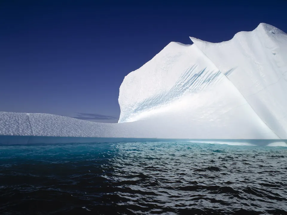 A colossal iceberg floats above choppy, deep blue ocean water.