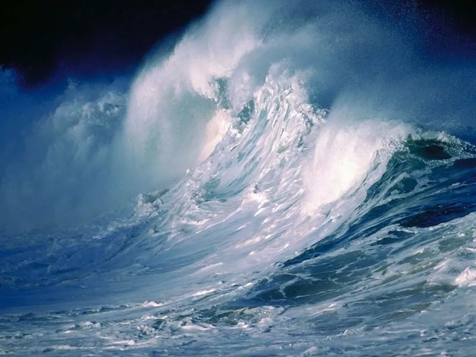 A powerful ocean wave crashes, with white foam and spray against a dark sky.