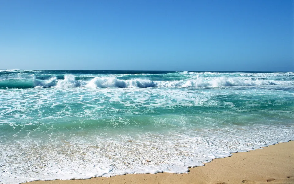 Waves crash on a sandy beach under a clear blue sky.