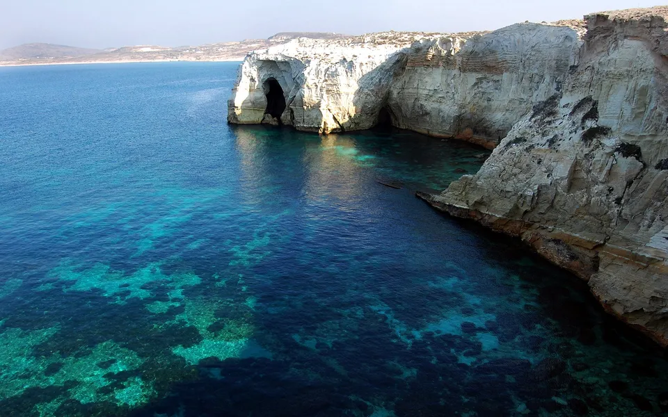 A view of turquoise water lapping against white cliffs with sea caves.