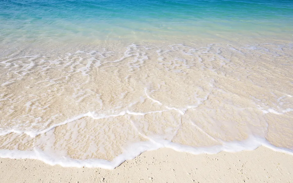 Crystal clear turquoise water gently washes over a light sandy beach, creating delicate patterns of foam.