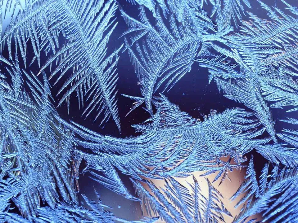 Intricate ice crystals forming delicate, fern-like patterns on a window.