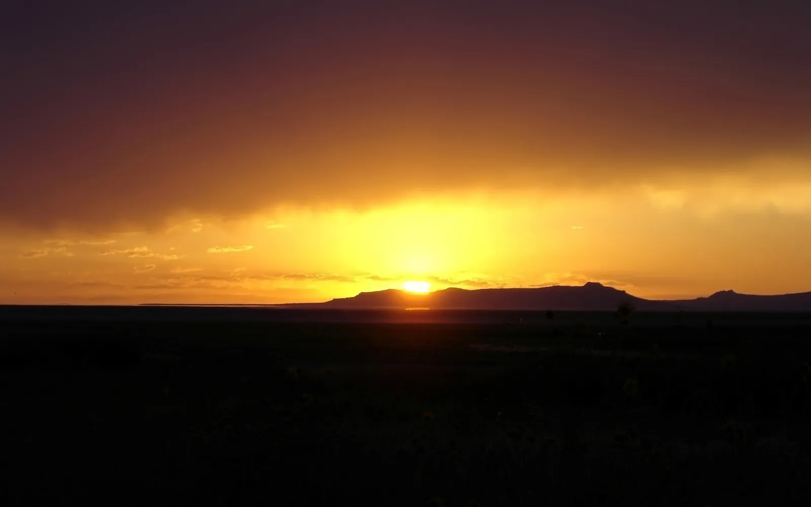 A vibrant sunset with golden light illuminating the sky over silhouetted desert mountains.