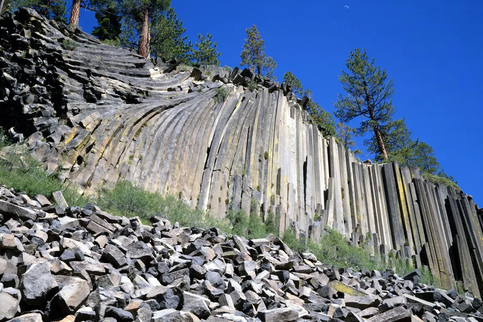 A cliff face composed of hexagonal basalt columns under a clear blue sky.