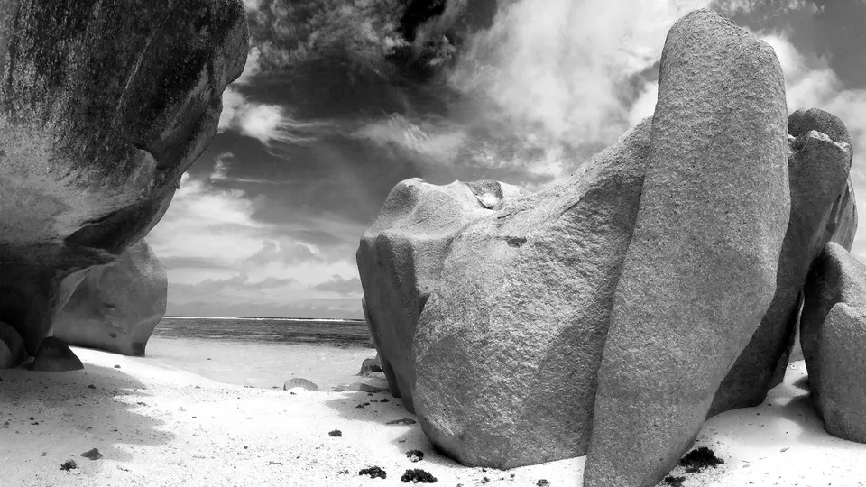 Black and white image of large granite boulders on a beach with dramatic clouds.