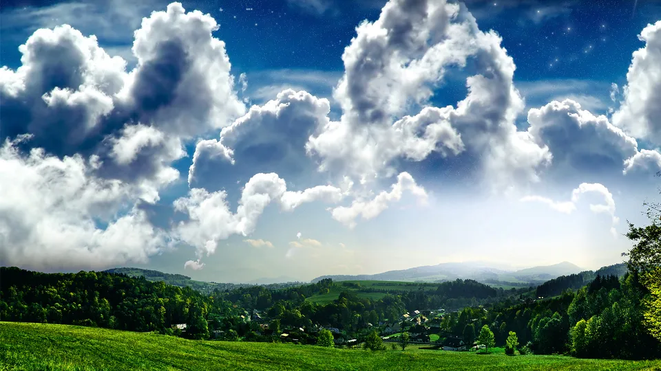 A panoramic view of large, fluffy cumulus clouds against a blue sky with visible stars, above a lush green landscape with rolling hills and a small village.