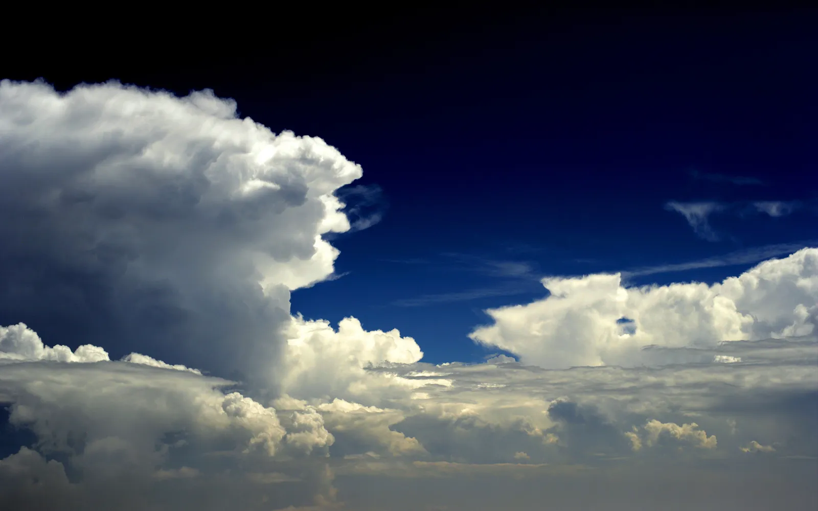 Large, white cumulonimbus clouds dominate the frame against a deep blue sky, with smaller clouds below.
