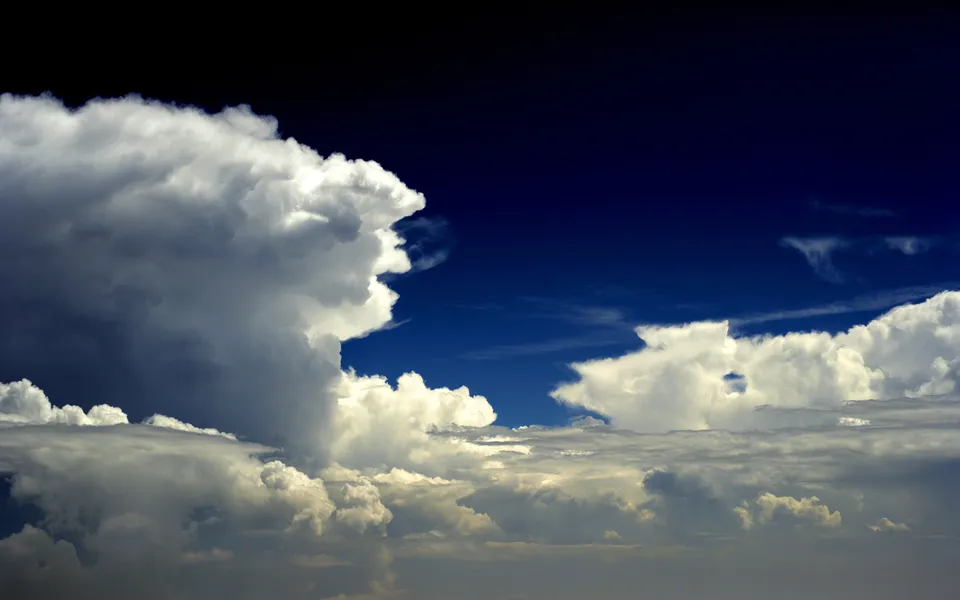 Large, white cumulonimbus clouds dominate the frame against a deep blue sky, with smaller clouds below.