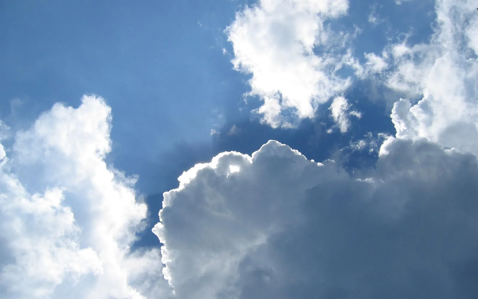 Large, fluffy cumulus clouds fill the sky, with some backlit by the sun.