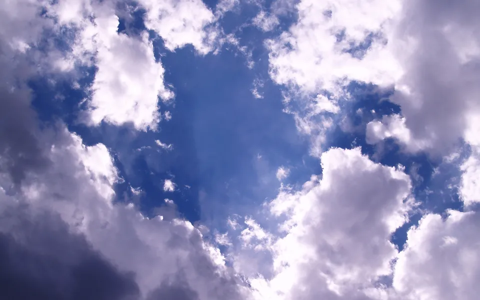 A view looking up at a deep blue sky filled with white and gray cumulus clouds.