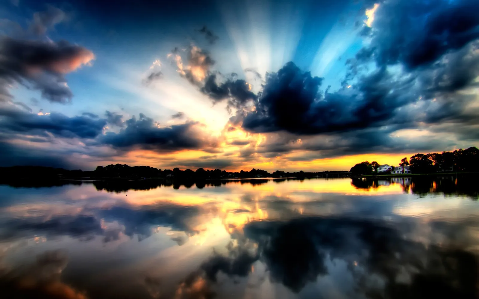 Sun rays burst through dark clouds over a reflective lake at sunset.
