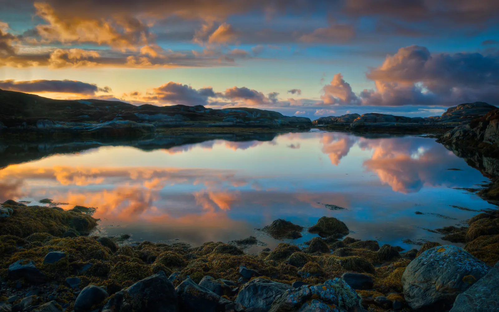 Dramatic sunset clouds reflected on the still water of a coastal inlet.