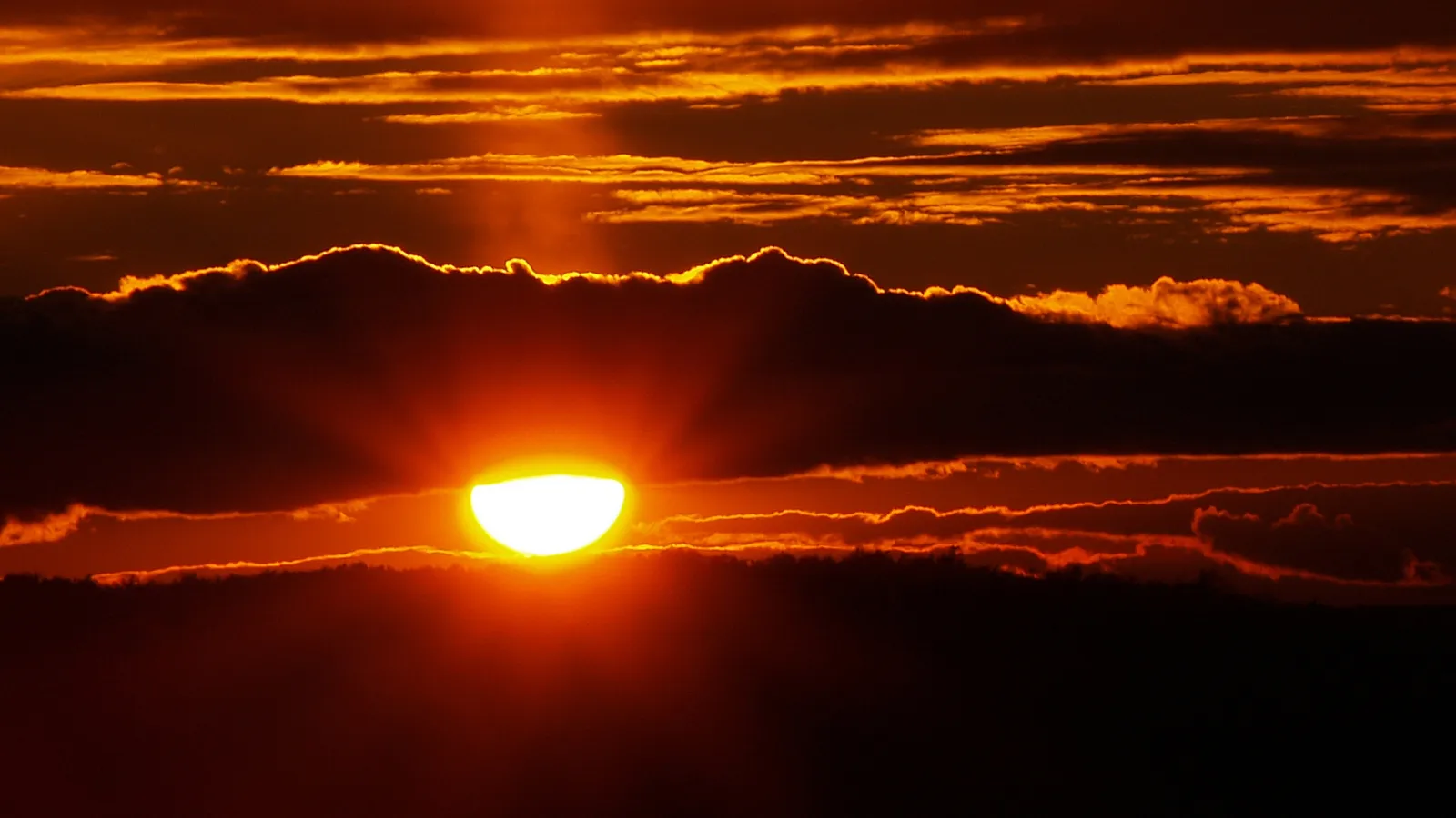 The sun is setting behind dark clouds, casting a bright orange glow through the sky.