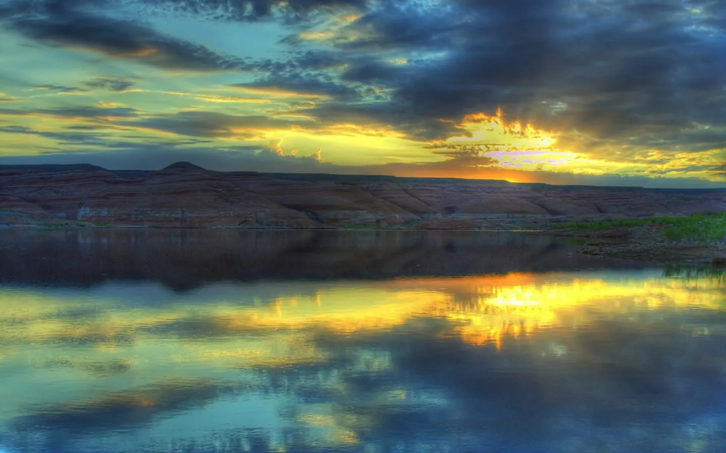 A vibrant sunset illuminates dramatic clouds over rugged hills and a reflective lake.