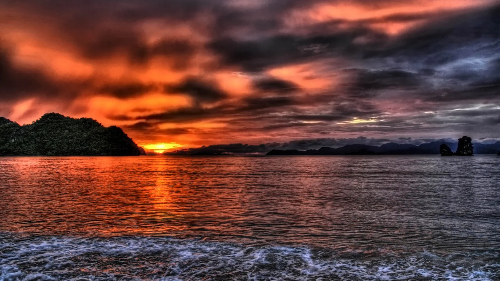 Dramatic sunset over the ocean with silhouetted islands on the horizon.