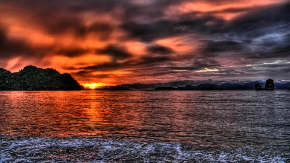 Dramatic sunset over the ocean with silhouetted islands on the horizon.