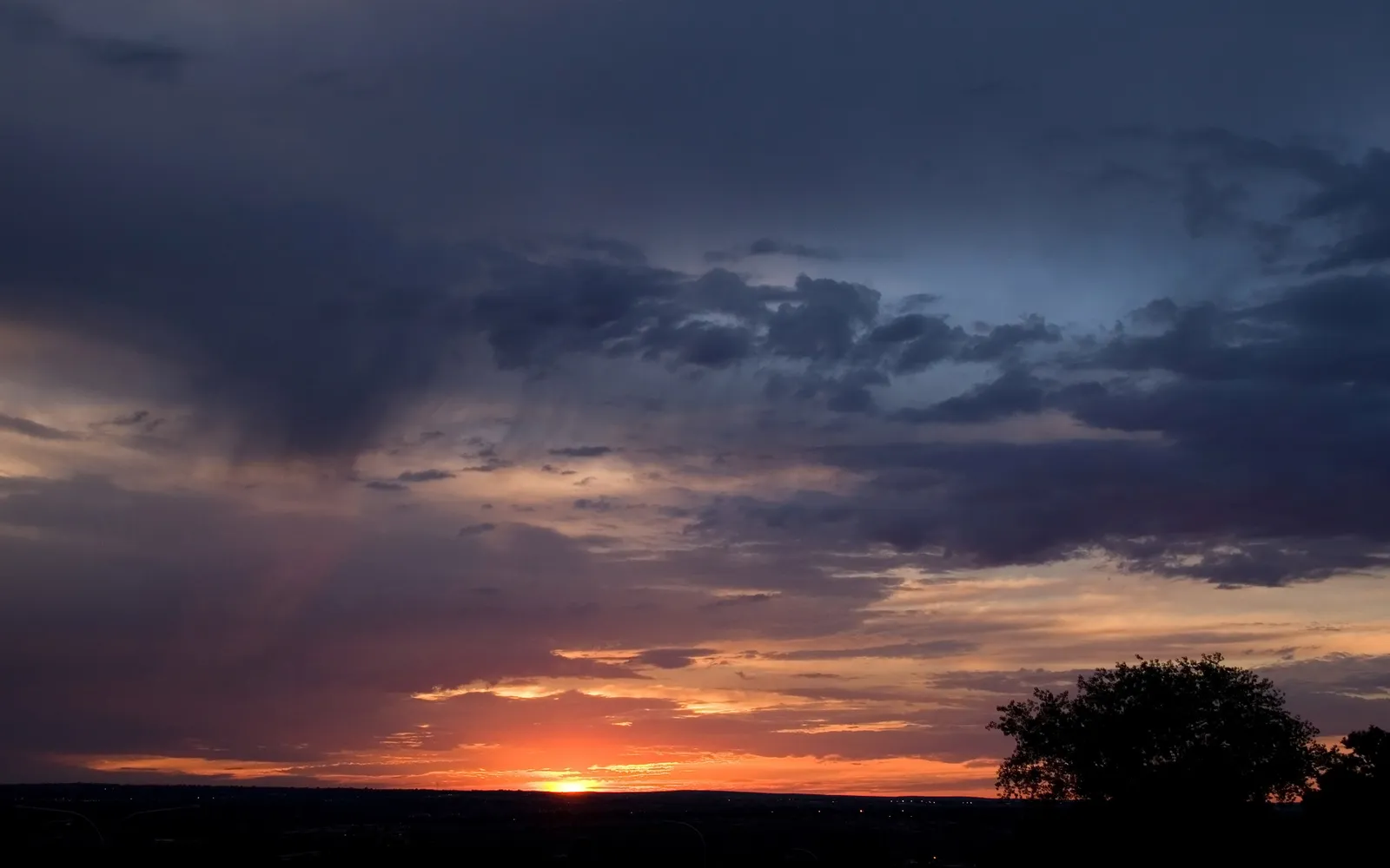 A dramatic sunset sky with dark clouds and bright orange and pink hues, with visible sun rays.