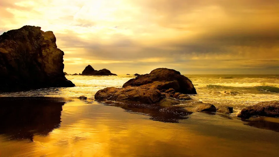 Dramatic clouds fill the sky above a rocky shoreline during a golden hour sunset.