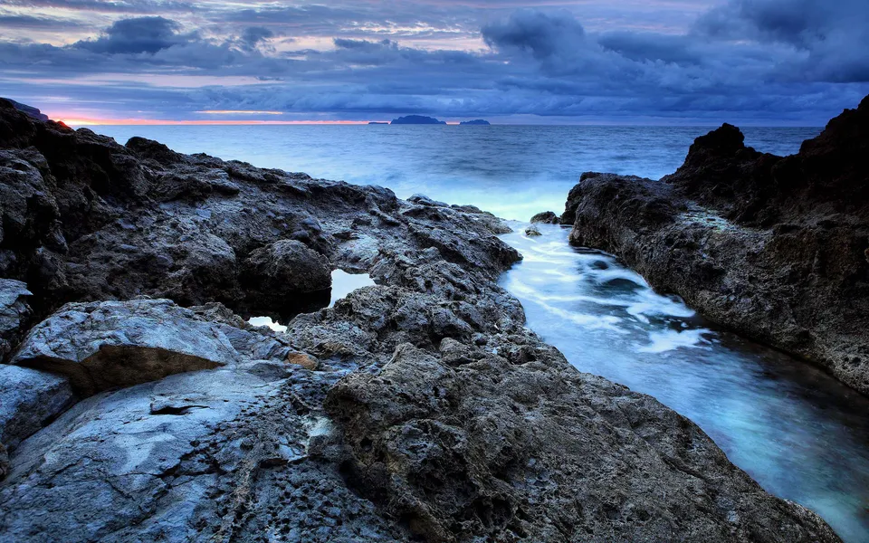 A rugged coastline at sunset with dramatic clouds and the ocean stretching to the horizon.