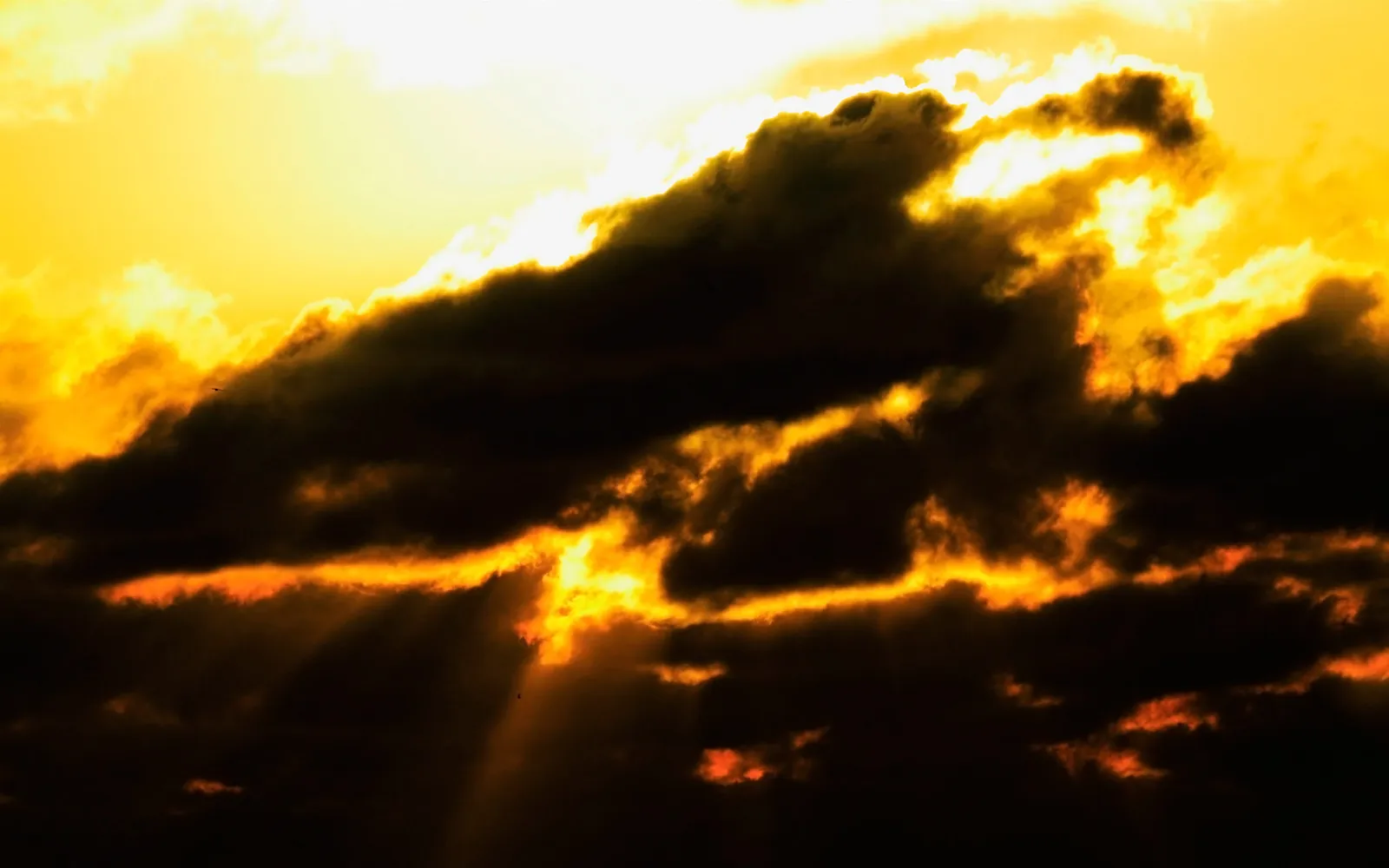 Dark clouds are illuminated by bright orange sunbeams breaking through during a dramatic sunset.