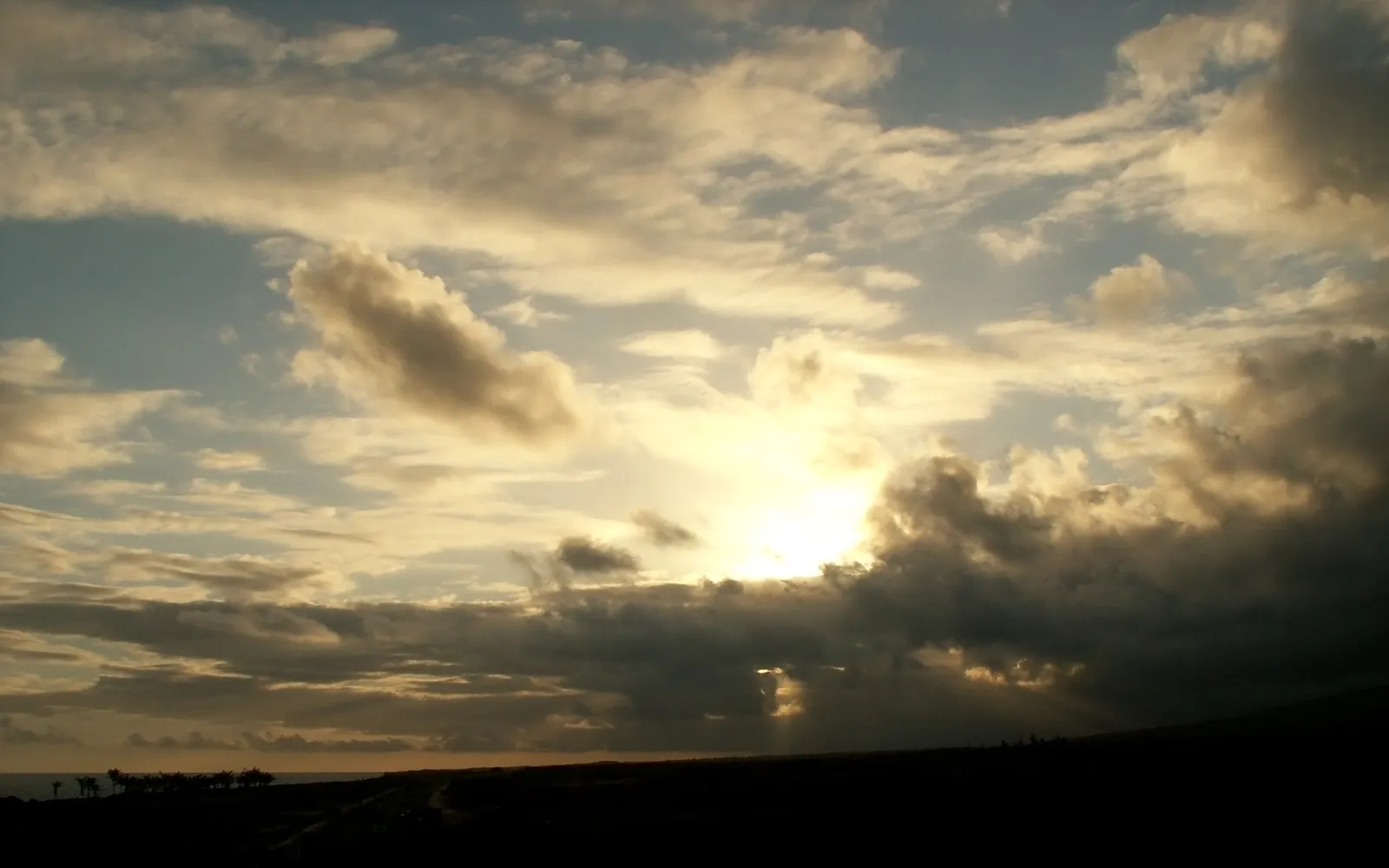 The sun breaks through dark clouds, casting golden rays over a silhouetted landscape.