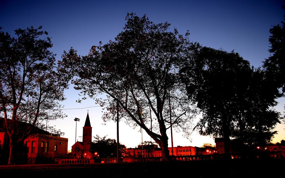 Silhouetted trees and buildings against a deep blue and orange dusk sky.