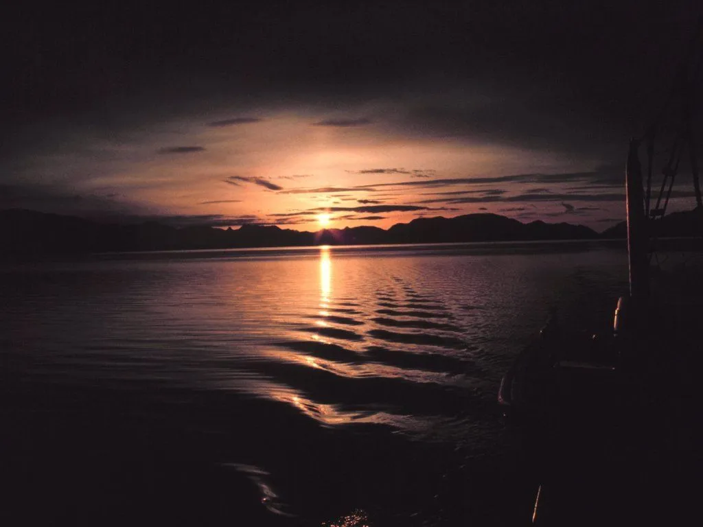 A dusk sunset over a calm body of water with mountains silhouetted on the horizon.