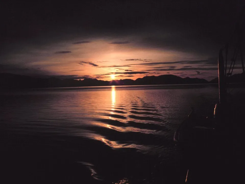A dusk sunset over a calm body of water with mountains silhouetted on the horizon.