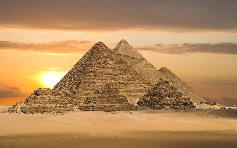 The Great Pyramids of Giza stand tall against a dramatic sunset sky with clouds.