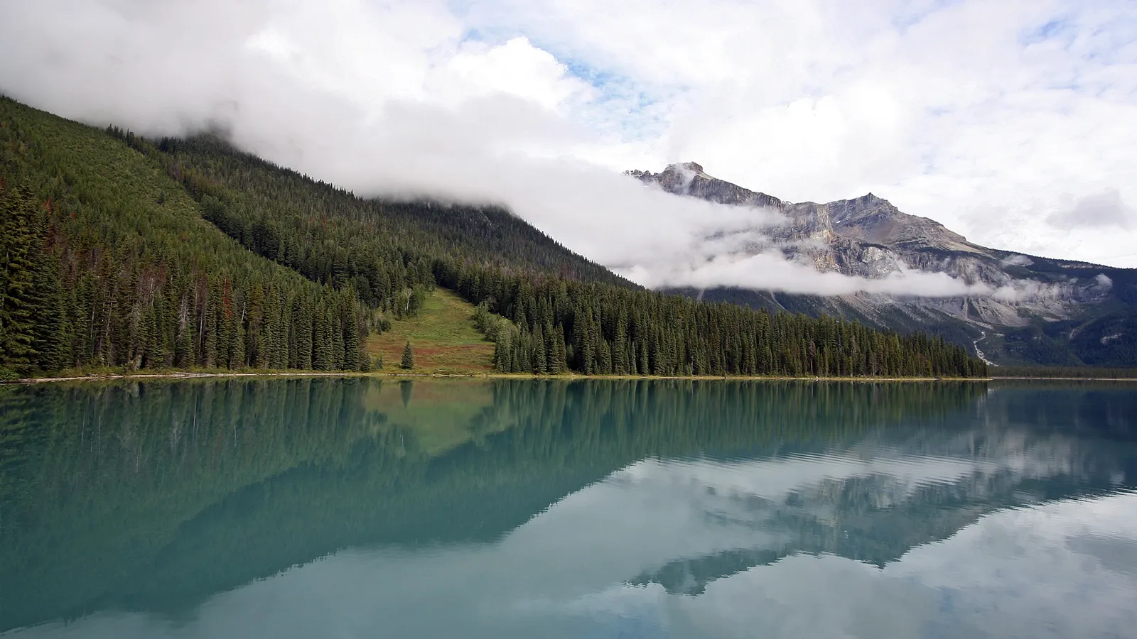 A turquoise lake reflects forested mountainsides and clouds in Banff National Park.
