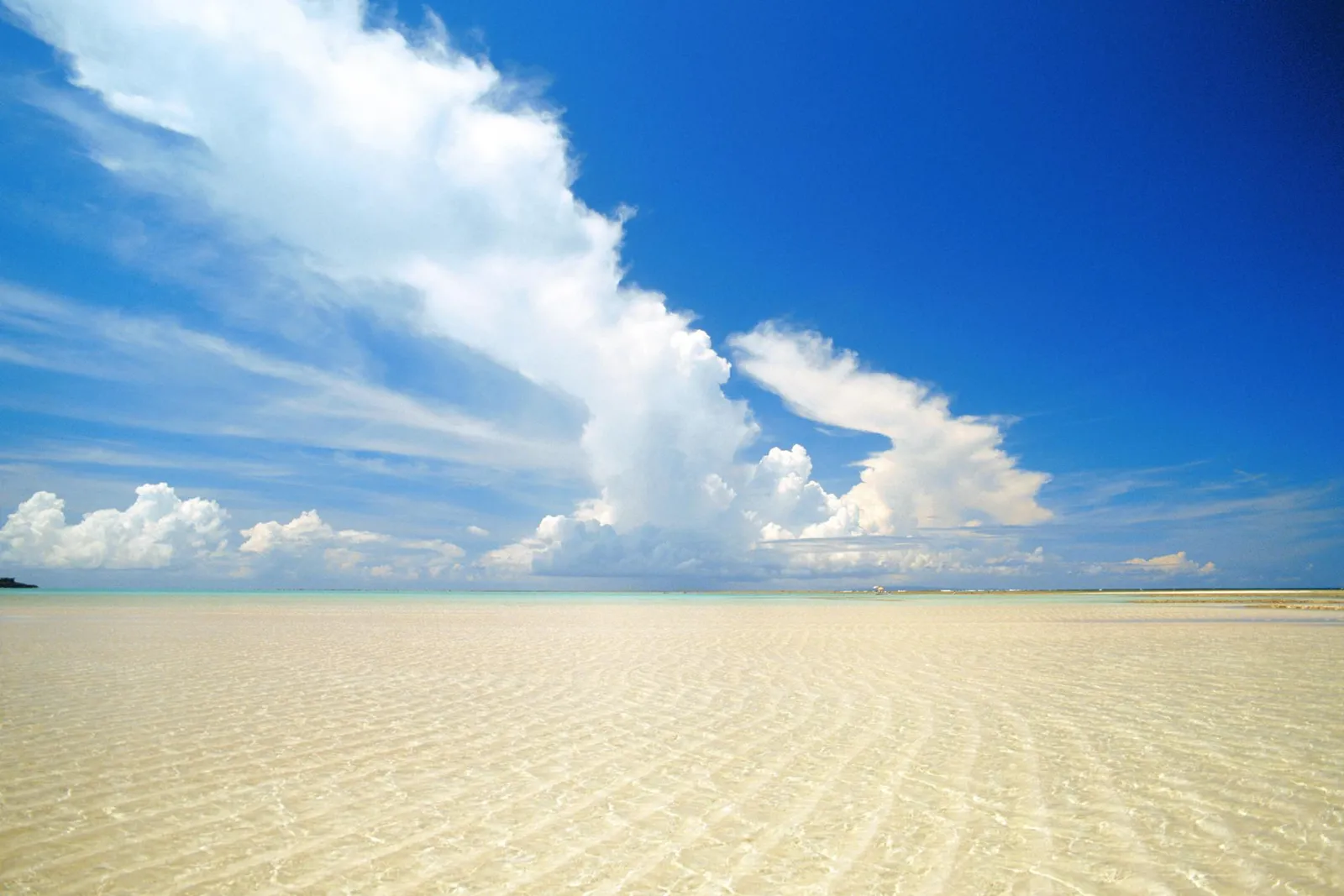 A wide, flat sandy beach with shallow water reflecting the sky and clouds.