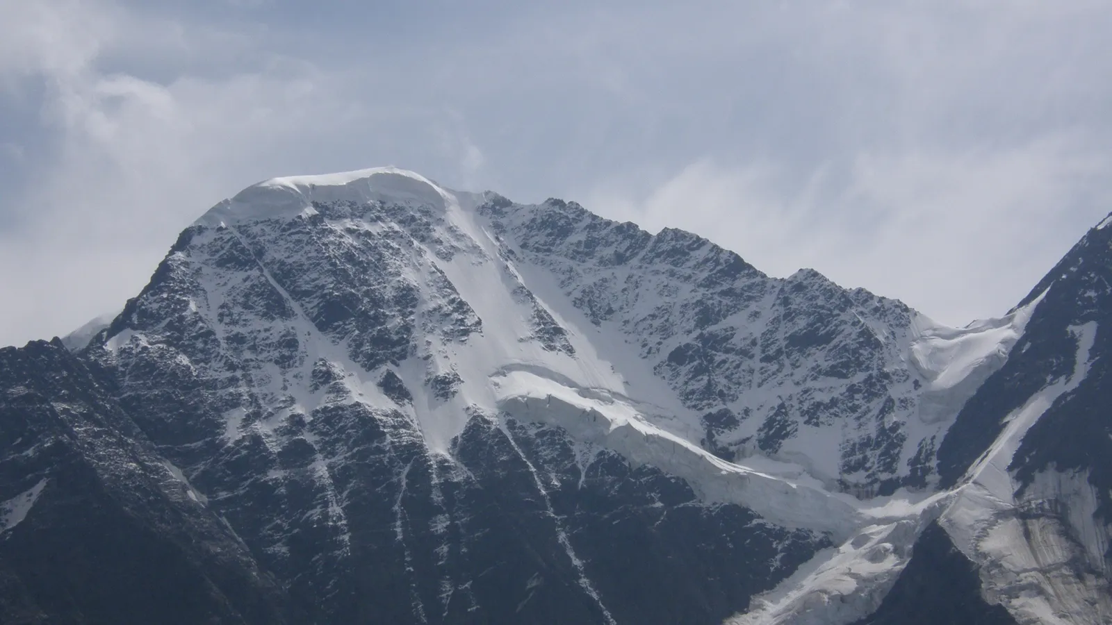 A vast mountain range is covered in snow and glaciers under a soft, overcast sky.