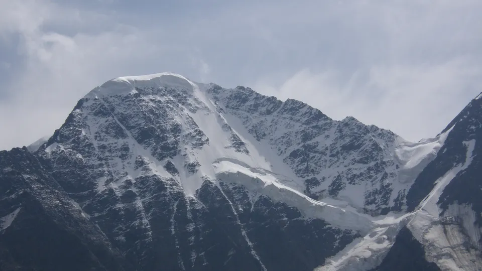 A vast mountain range is covered in snow and glaciers under a soft, overcast sky.