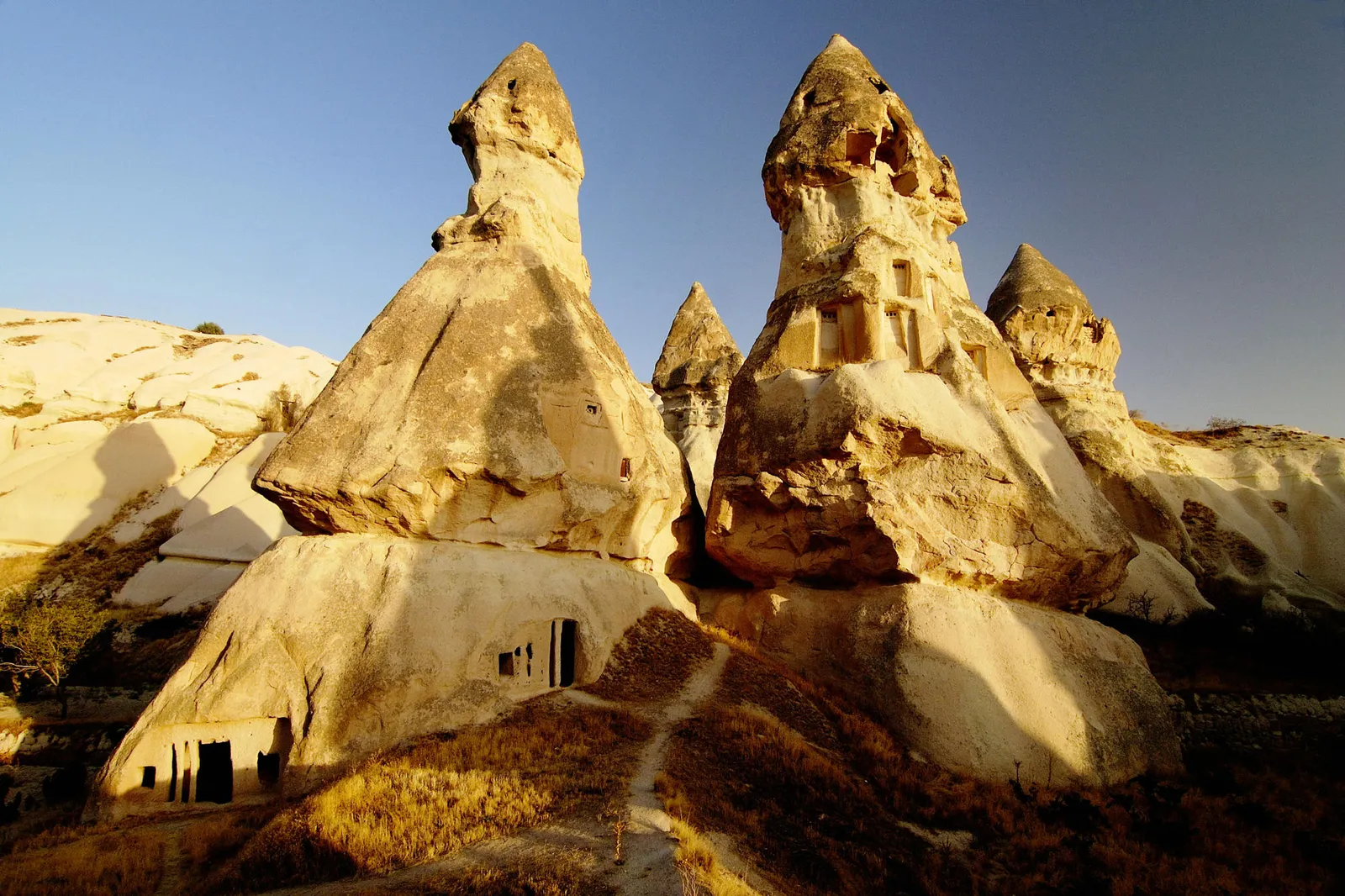 Unique rock formations with carved dwellings, illuminated by warm sunlight under a clear blue sky.