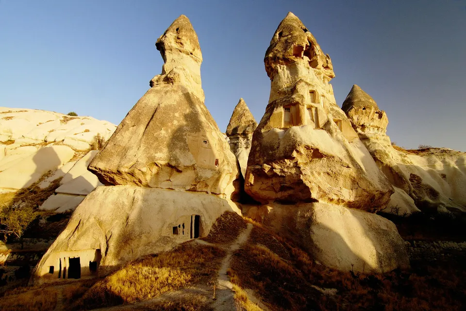Unique rock formations with carved dwellings, illuminated by warm sunlight under a clear blue sky.